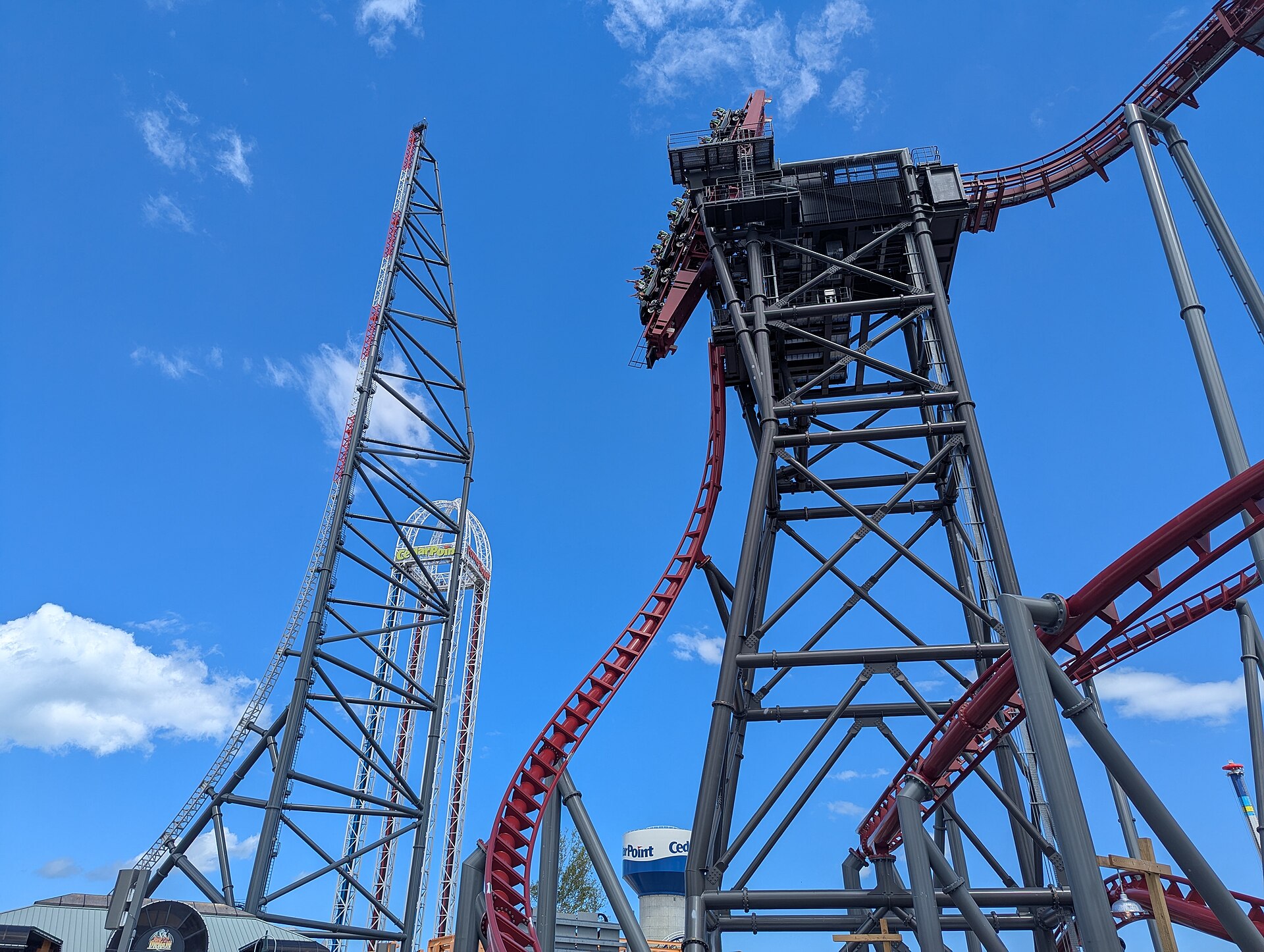 Top Thrill 2's tower and Siren's Curse's tilting track side by side at Cedar Point under a deep blue sky