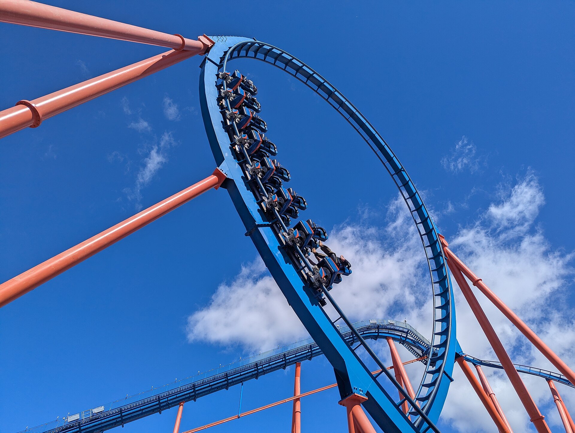 A full Scream! train going over the top of its blue vertical loop, riders upside down, against a deep blue sky at Six Flags Magic Mountain