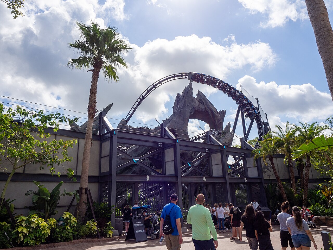 VelociCoaster's dark track arching over its rock gateway, palm trees in front
