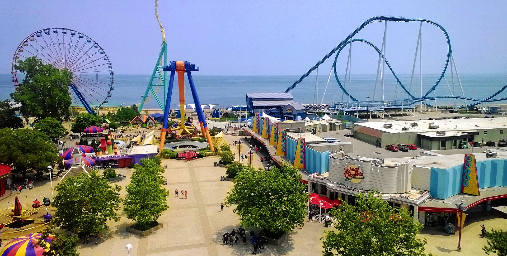 Cedar Point from the Sky Ride: the midway, the Giant Wheel and GateKeeper's blue loops along the beach, Lake Erie behind, under a blue sky