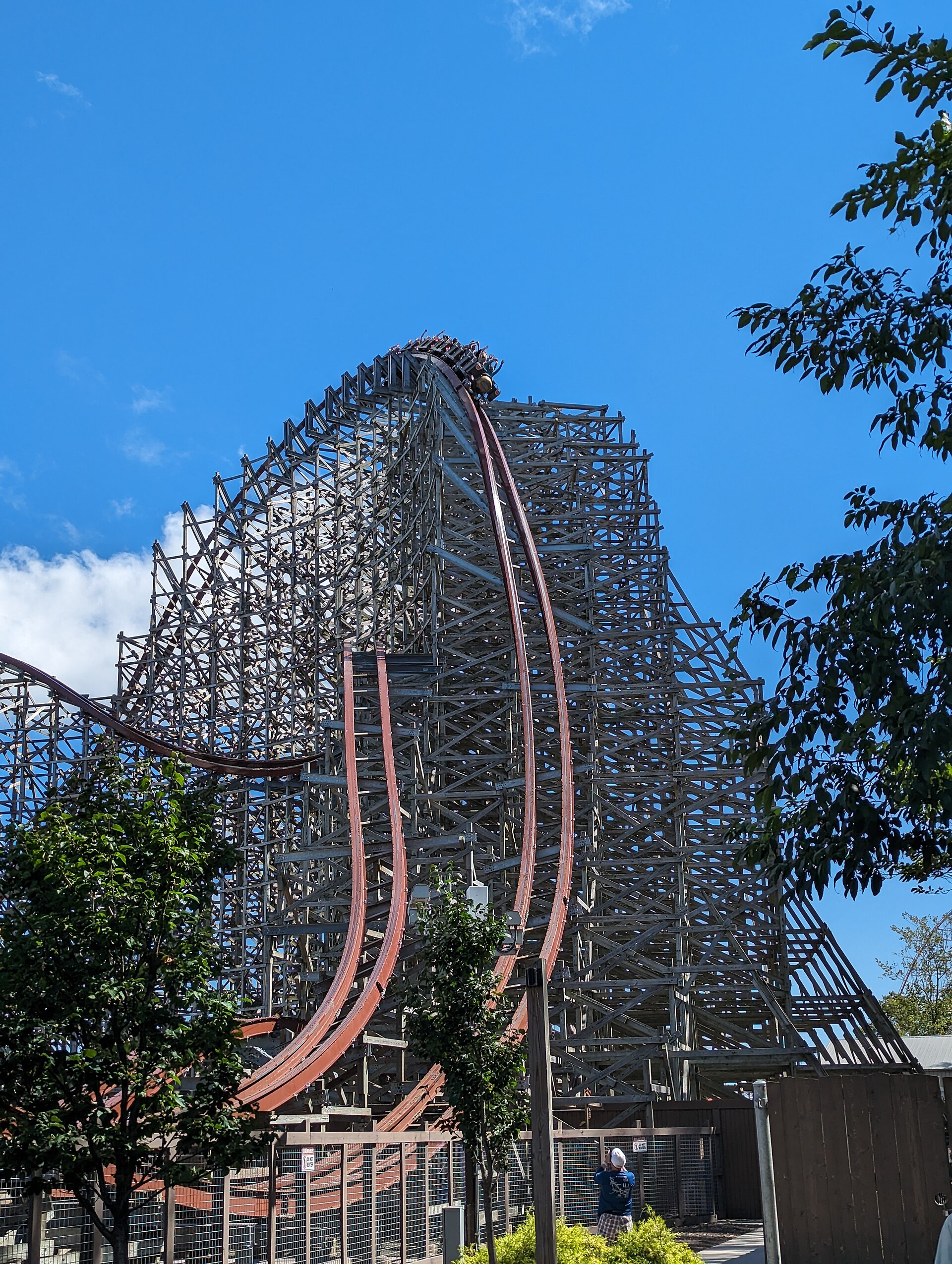 A Steel Vengeance train cresting the top of the first drop above its gray wooden structure, blue sky behind