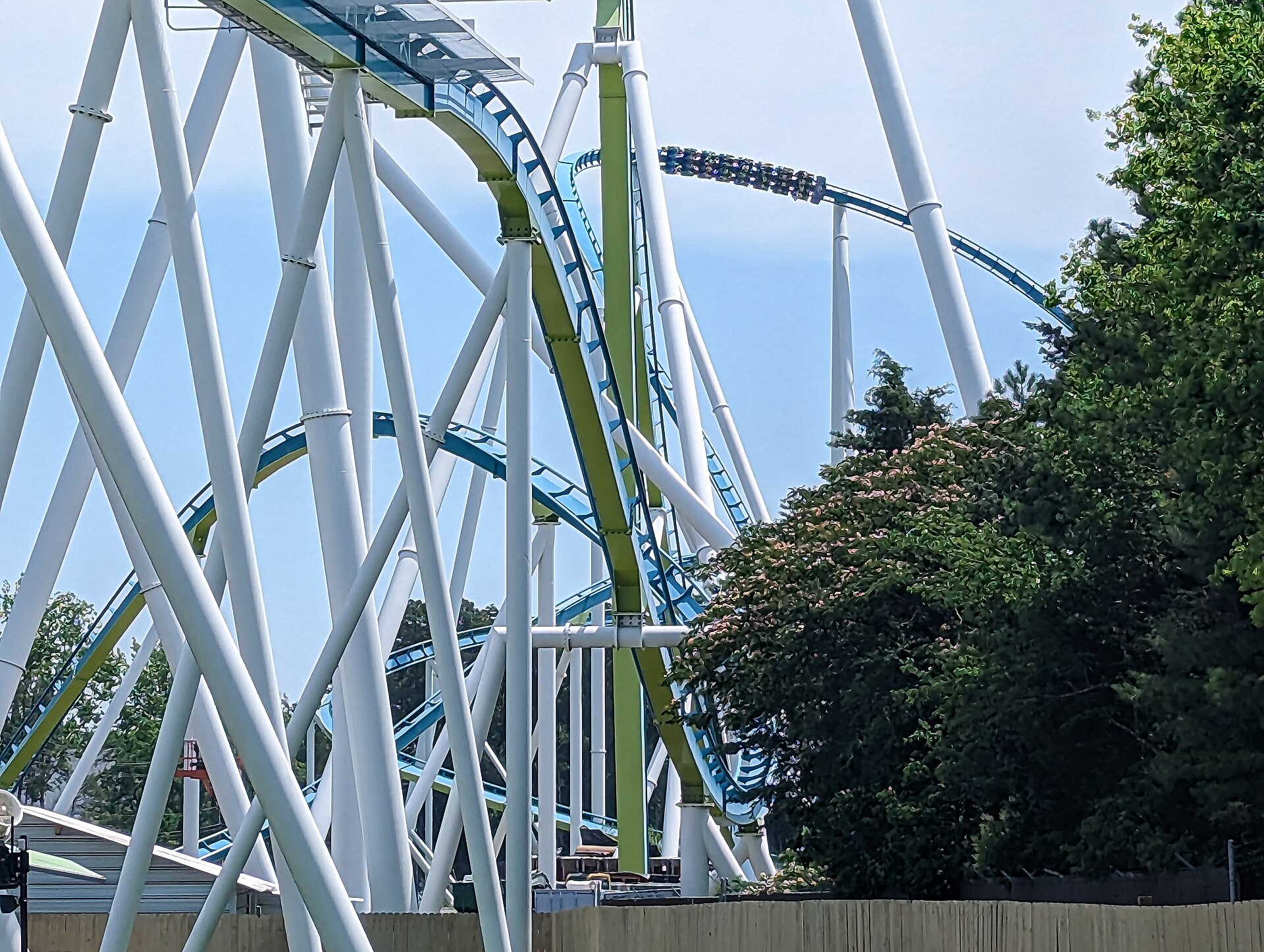 A Fury 325 train on its green track between the tall white supports, trees beside it