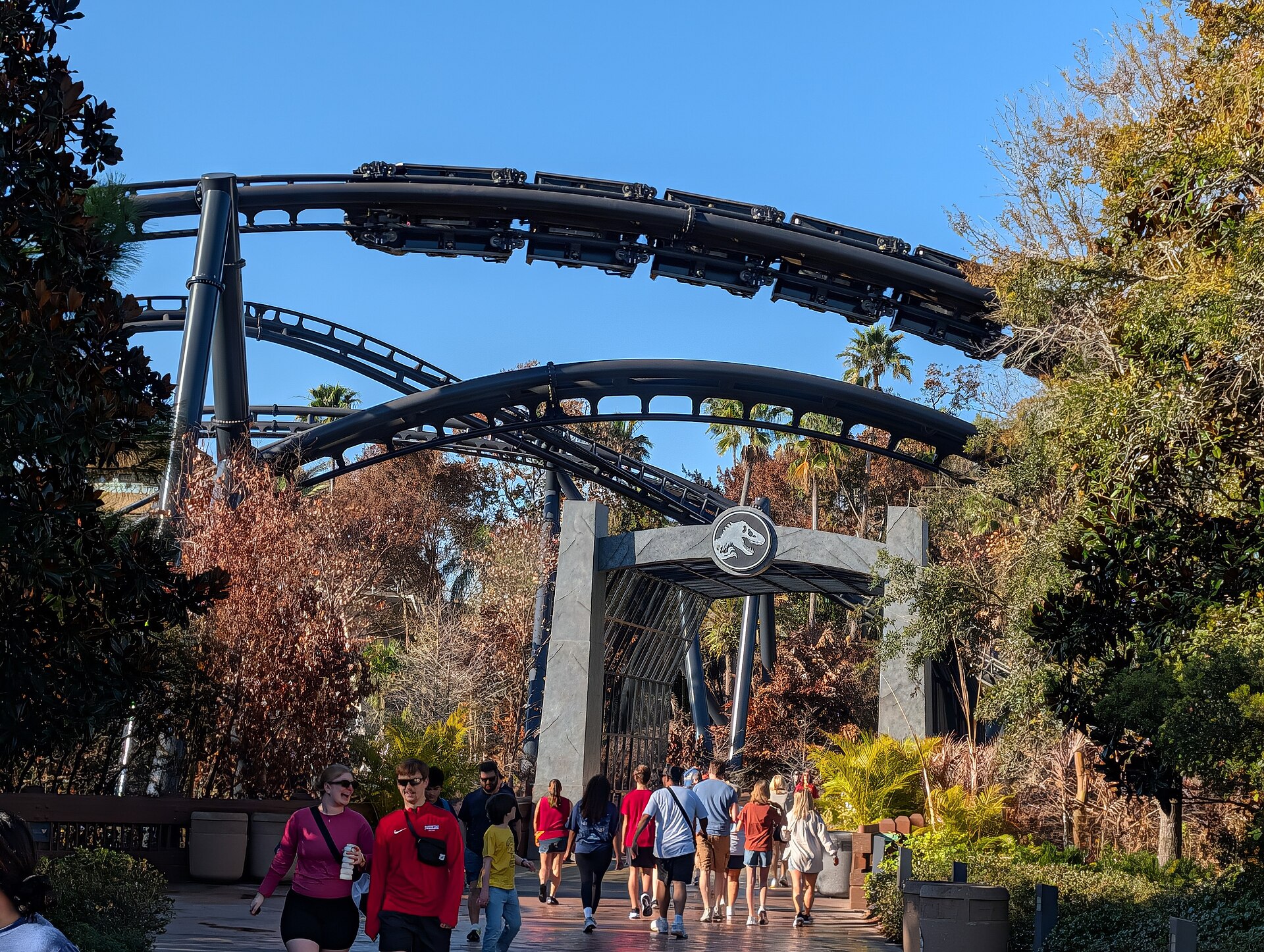 A VelociCoaster train hanging upside down in its stall over the arch at the ride's gate, a second arch of track below it, under a clear blue sky